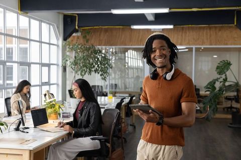 Smiling african american man holding tablet in modern coworking space with diverse team