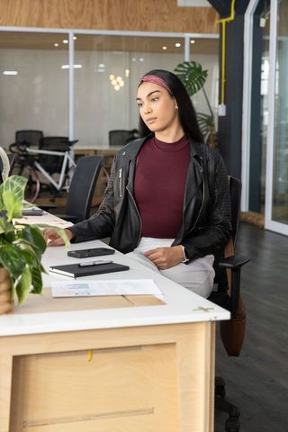 Young professional woman working at modern coworking desk with leather jacket and notebook