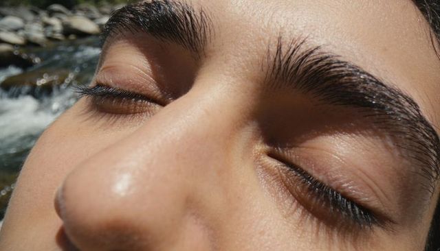 Male face relaxing by stream, macro closeup showing eyelashes skin texture pores and sunlight