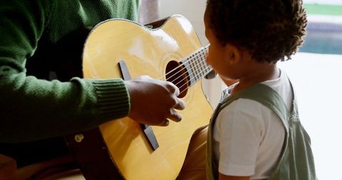 Man in Green Sweater Teaching Toddler Guitar at Home