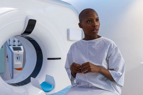 African female patient sitting beside ct scanner wearing hospital gown looking thoughtful