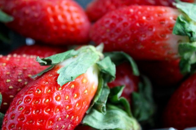 High-quality close-up of fresh strawberries with green leaves, showcasing their vibrant red color and lush green tops. Ideal for use in agriculture promotions, dietary content, blogs on organic farming, health food publications, and cooking recipes.