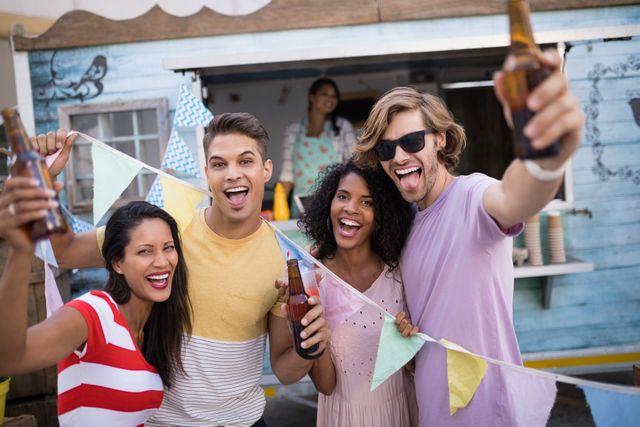 Group of friends enjoying a casual outdoor celebration near a food truck, holding beer bottles and smiling. Perfect for themes related to social gatherings, summer parties, friendship, and leisure activities. Ideal for advertisements, social media posts, and lifestyle blogs focusing on fun and community.