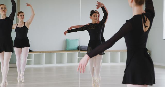 Professional ballet dancers gracefully practicing in a dance studio with mirrors, wearing matching black leotards and pointe shoes. Ideal for content related to dance education, performing arts, ballet training, elegance in motion, and physical fitness. Perfect for dance school brochures, performing arts promotions, and articles on ballet techniques and practices.