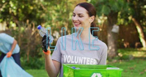 Smiling volunteer collecting plastic bottle for recycling during park cleanup, green bin