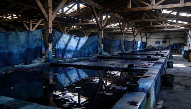 Indigo dye vats in rustic workshop with hanging blue fabrics