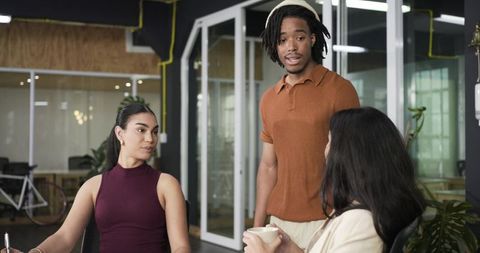 Young diverse team collaborating in modern glass office during casual brainstorming session