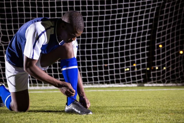 Male soccer player tying shoelace against goal post on soccer field