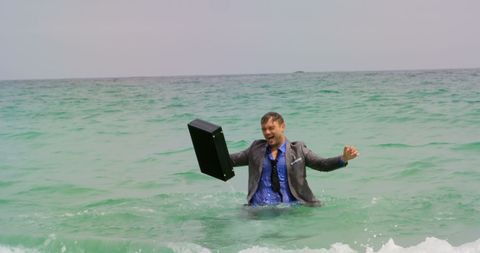 Joyful businessman dancing in ocean with briefcase