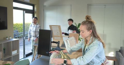 Friends assembling home office desk, woman unwrapping brass lamp, team collaboration