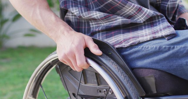 This portrays a close-up view of a man's hand as he operates a wheelchair outdoors. It highlights themes of mobility, independence, and daily life. Suitable for use in articles, blogs, and educational materials about disabilities, assistive devices, and personal independence.