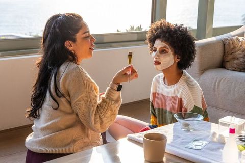 Sunlit self-care ritual: diverse friends applying facial mask in cozy living room