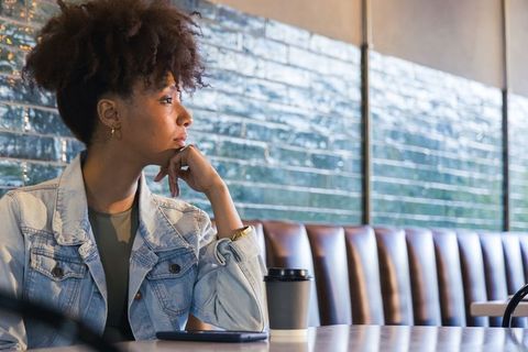 Contemplative african american woman sitting in urban cafe gazing left with coffee cup