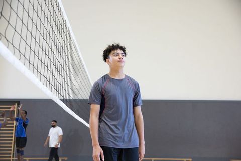 Teen volleyball player standing by net during indoor practice showing focus for team