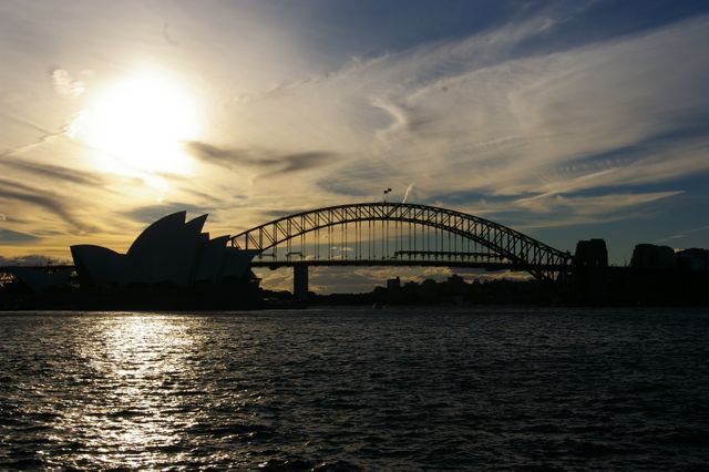 View of Sydney Harbour Bridge and Sydney Opera House at sunset with sky and water in the foreground. Perfect for travel blogs, tourism brochures, and promotional materials to attract visitors to Sydney. Highlights iconic Australian landmarks and scenic waterfront.