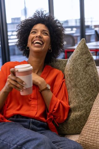 Smiling woman in orange blouse relaxing in office lounge with coffee