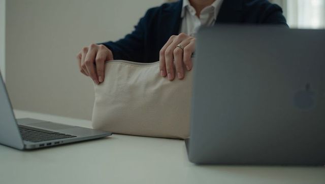 Business professional holding beige pouch between laptops on minimalist white desk