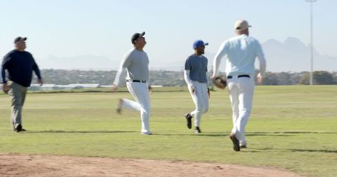 Men jogging and walking on sunny baseball field carrying gloves and caps during practice