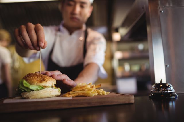 Chef placing tooth pick over burger at order station in the commercial kitchen