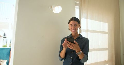 Casual Woman Smiling at Phone Near Hallway Lamp