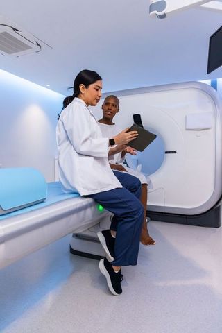 Female clinician consulting with patient at ct scanner using tablet for diagnostic review