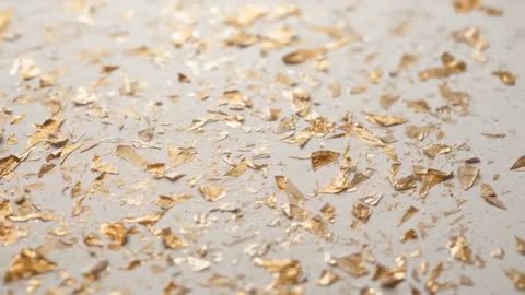 Gold leaf flakes scattering on cream tabletop while camera shifting focus revealing metallic texture