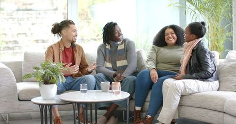 Diverse friends laughing and talking while sitting on sectional sofa in bright lounge