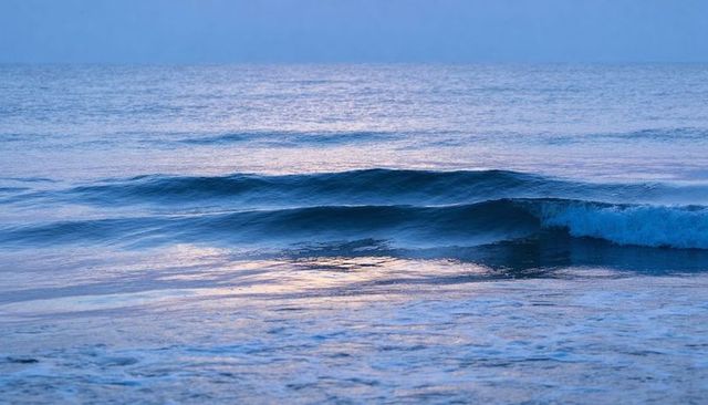 Pastel dawn ocean waves rolling toward shoreline with soft pink-blue reflections