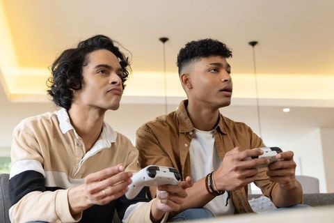 Young friends playing video games on couch holding controllers focused gaming duo