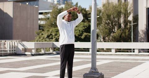 African american man stretching on urban rooftop deck near lamppost before workout