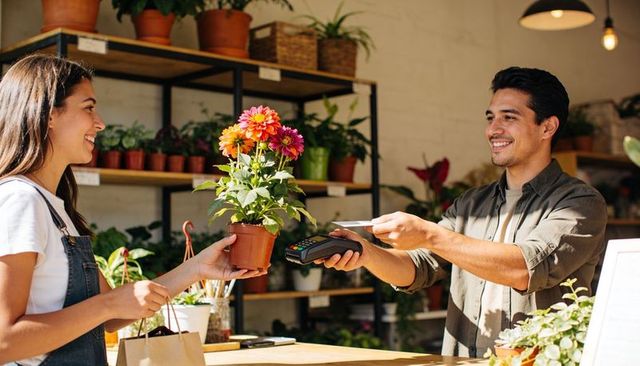 Smiling customer buying potted flower in local plant shop using contactless card payment
