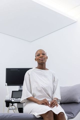 African woman patient sitting on exam table wearing medical gown beside diagnostic monitor