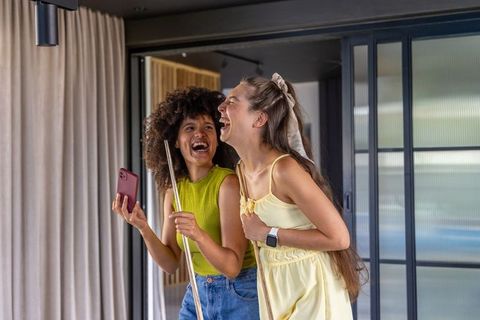 Laughing female friends holding pool cues and smartphone while enjoying casual game night