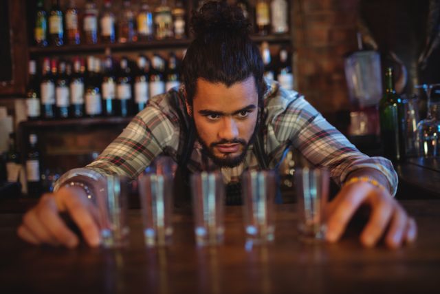 Waiter placing shot glasses in a row on counter in pub