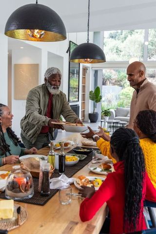 Multigenerational african american family sharing meal in modern sunlit open-plan dining room