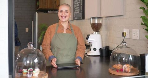 Smiling female barista holding tablet behind counter serving pastries in cozy cafe
