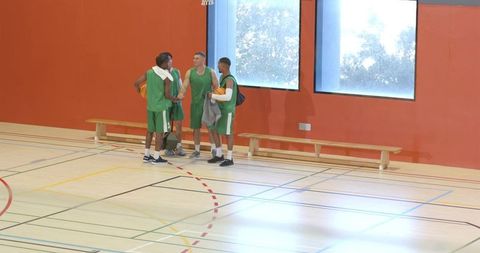 Diverse male basketball teammates huddling and walking from bench after timeout, holding basketball