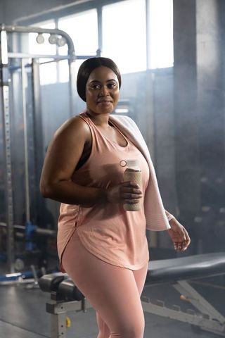 African-american woman working out in gym holding shaker bottle and towel wearing pink activewear