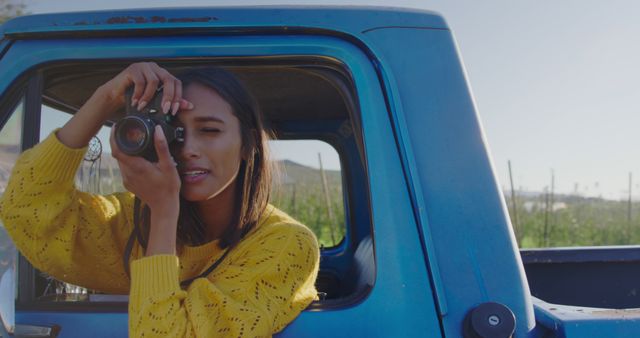 Young African American woman captures memories from a vintage truck, with copy space. She's outdoors, combining her passion for photography with a love for adventure.