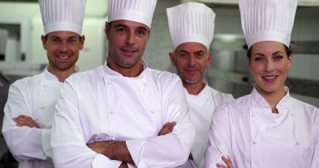 Four professional chefs in pristine white uniforms and chef hats posing confidently in a kitchen with arms crossed. Suitable for articles, websites, and promotional materials related to culinary arts, restaurant business, teamwork, and professional cooking.