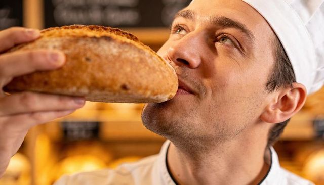 Baker inhaling aroma of rustic sourdough loaf in artisan bakery interior