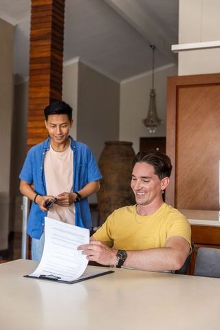 Asian and caucasian men reviewing rental agreement at home dining table, signing paperwork