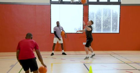 Coach supervising jump shot while teammate dribbling on bright indoor basketball court