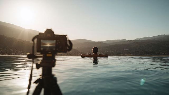 Capturing sunset over valley from infinity pool with camera on tripod and relaxing man