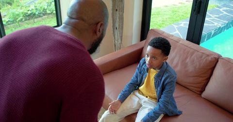 African american father confronting son on couch near pool tense parenting moment