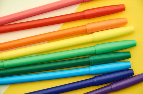Colorful pens arranged in spectrum on yellow background
