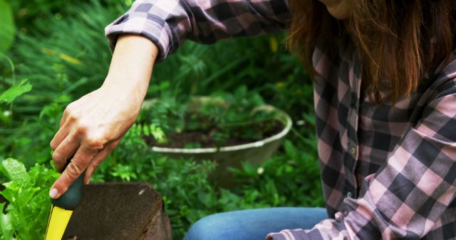 Woman wearing plaid shirt using trowel in outdoor garden. Perfect for depicting leisure activities, hobbies, summer gardening, nature scenes, and lifestyles centered around relaxation and outdoor activities.
