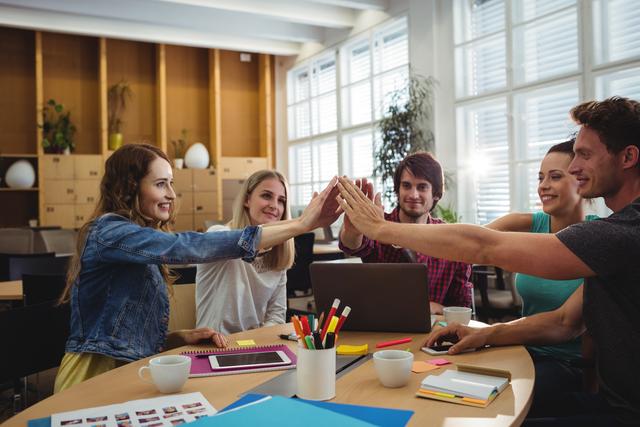 Young professionals in a modern office celebrating success with a high five. Ideal for illustrating teamwork, collaboration, and a positive work environment in business presentations, websites, and promotional materials for startups or corporate culture.