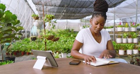 Woman Gardening Enthusiast Taking Notes in Greenhouse