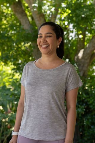 Smiling woman standing in sunlit backyard garden wearing casual gray knit top and smartwatch